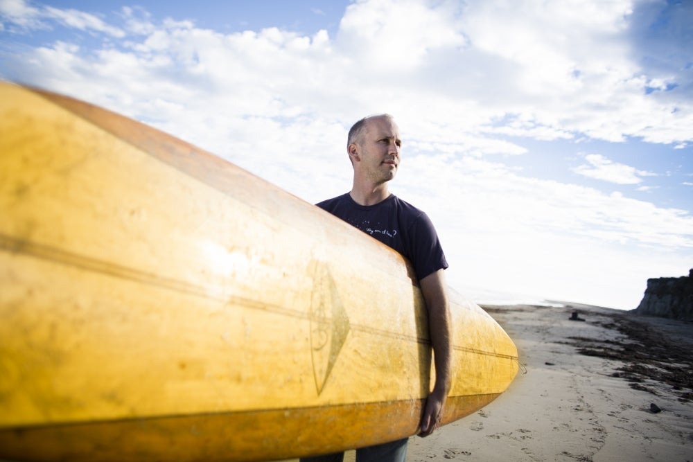 Man (Halpern) holding surfboard on the beach