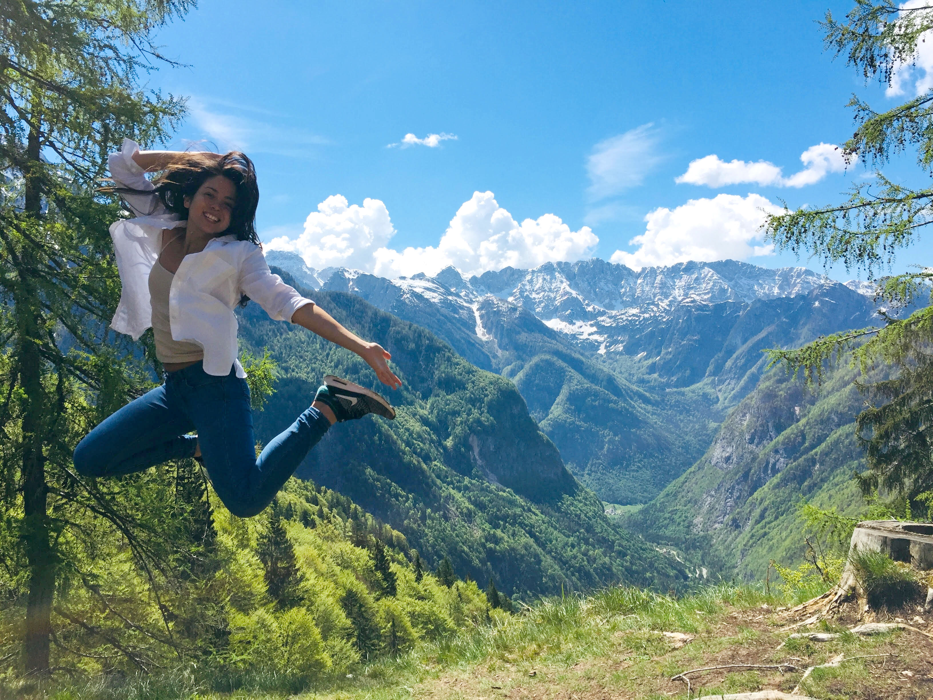 Woman jumping into air with forest mountain vista behind her