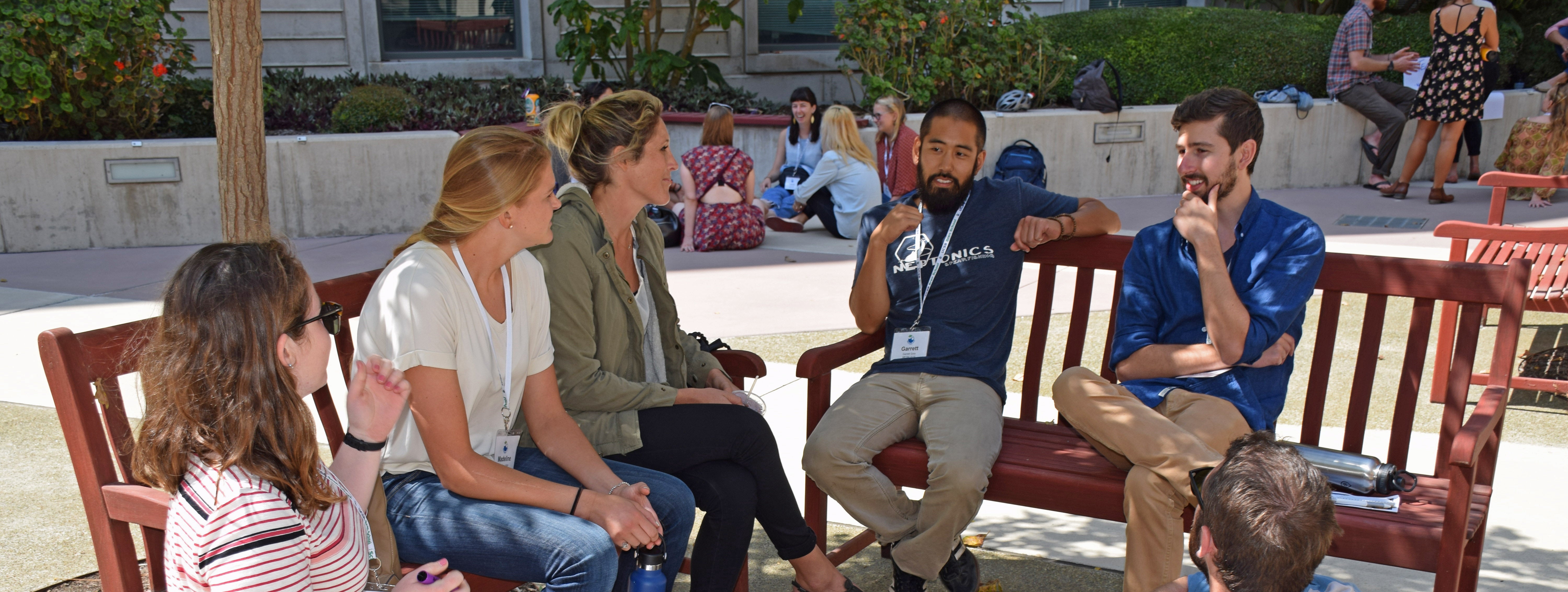 Five student sit on benches in courtyard talking