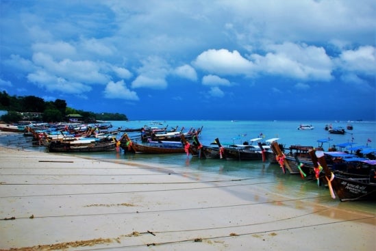 A line of fishing boats tethered to shore under a blue sky