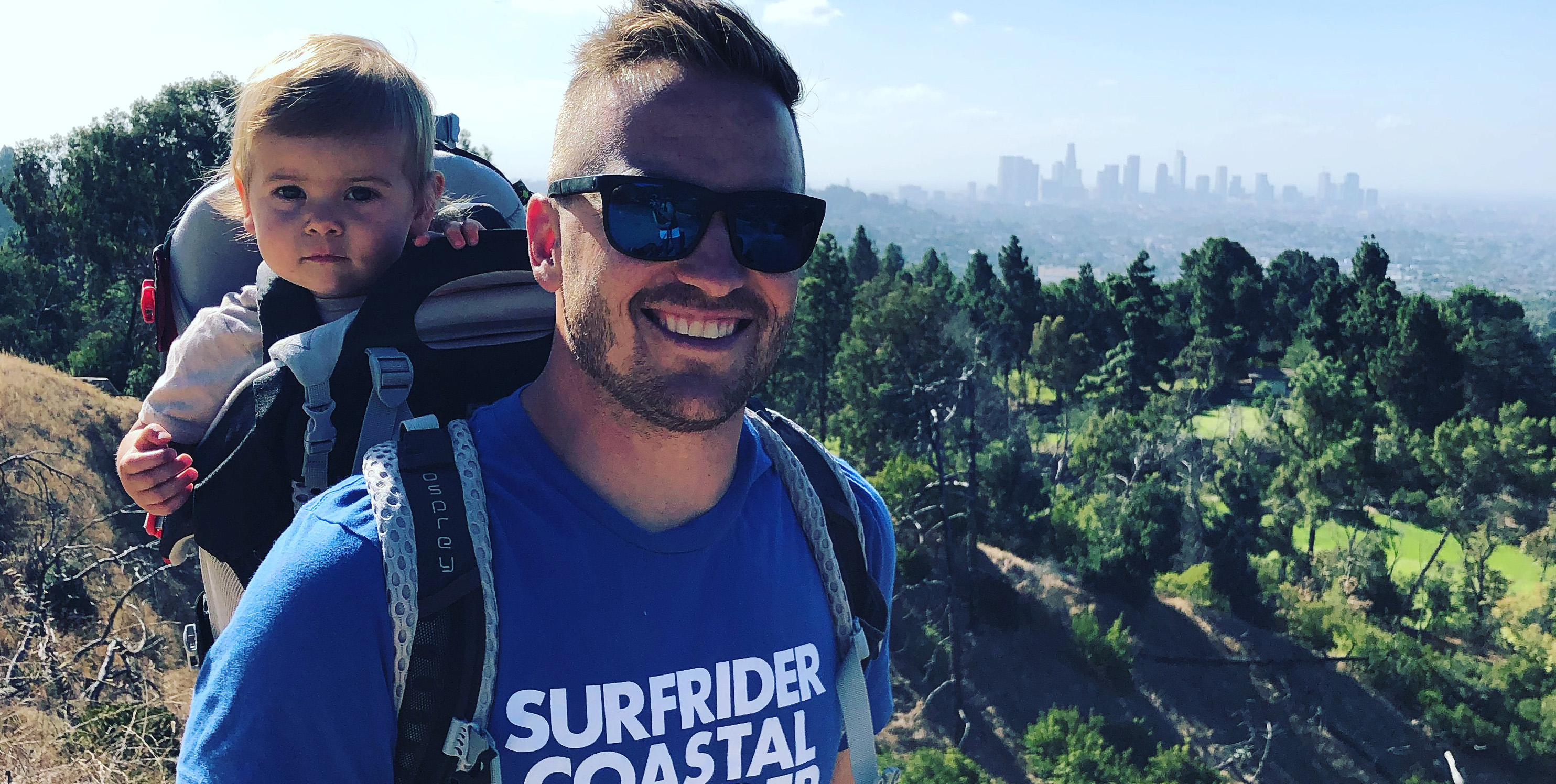 Hiking man with baby in backpack, city in distance