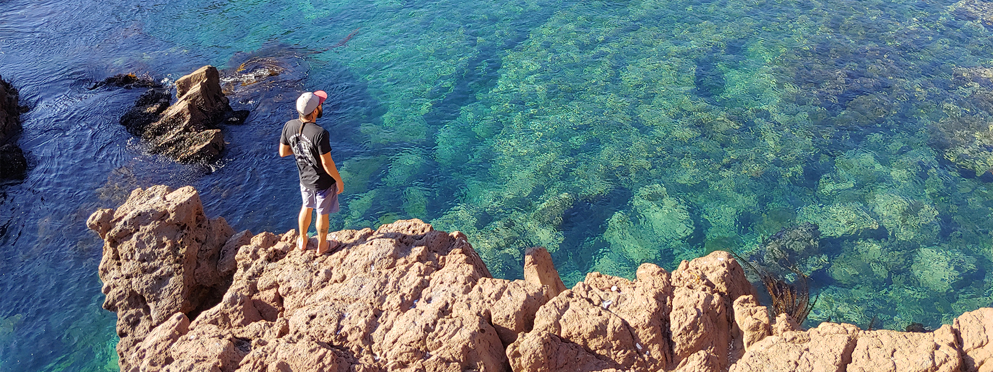 Man standing on rocks looking at clear ocean water