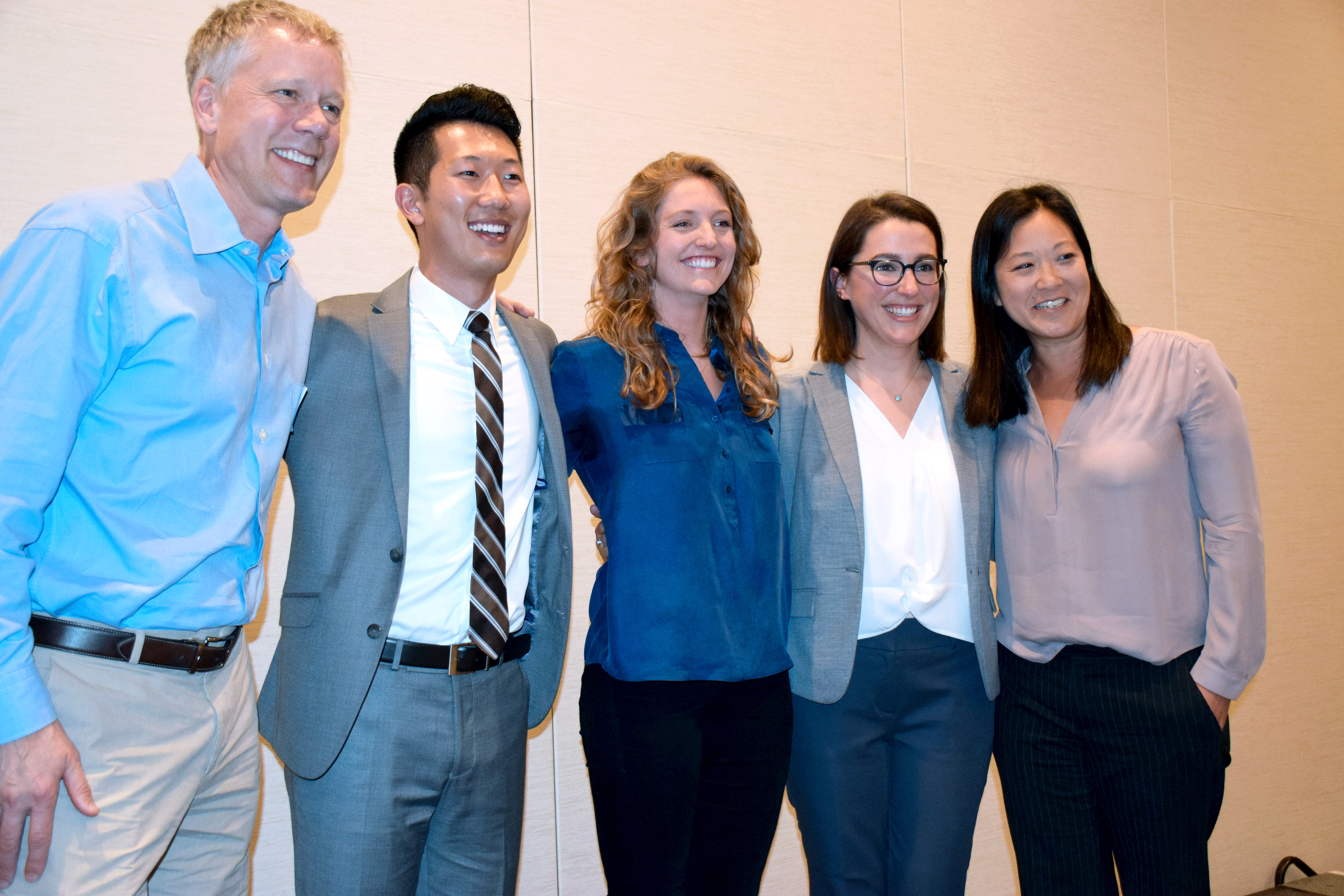 Five people link arms and smile on stage