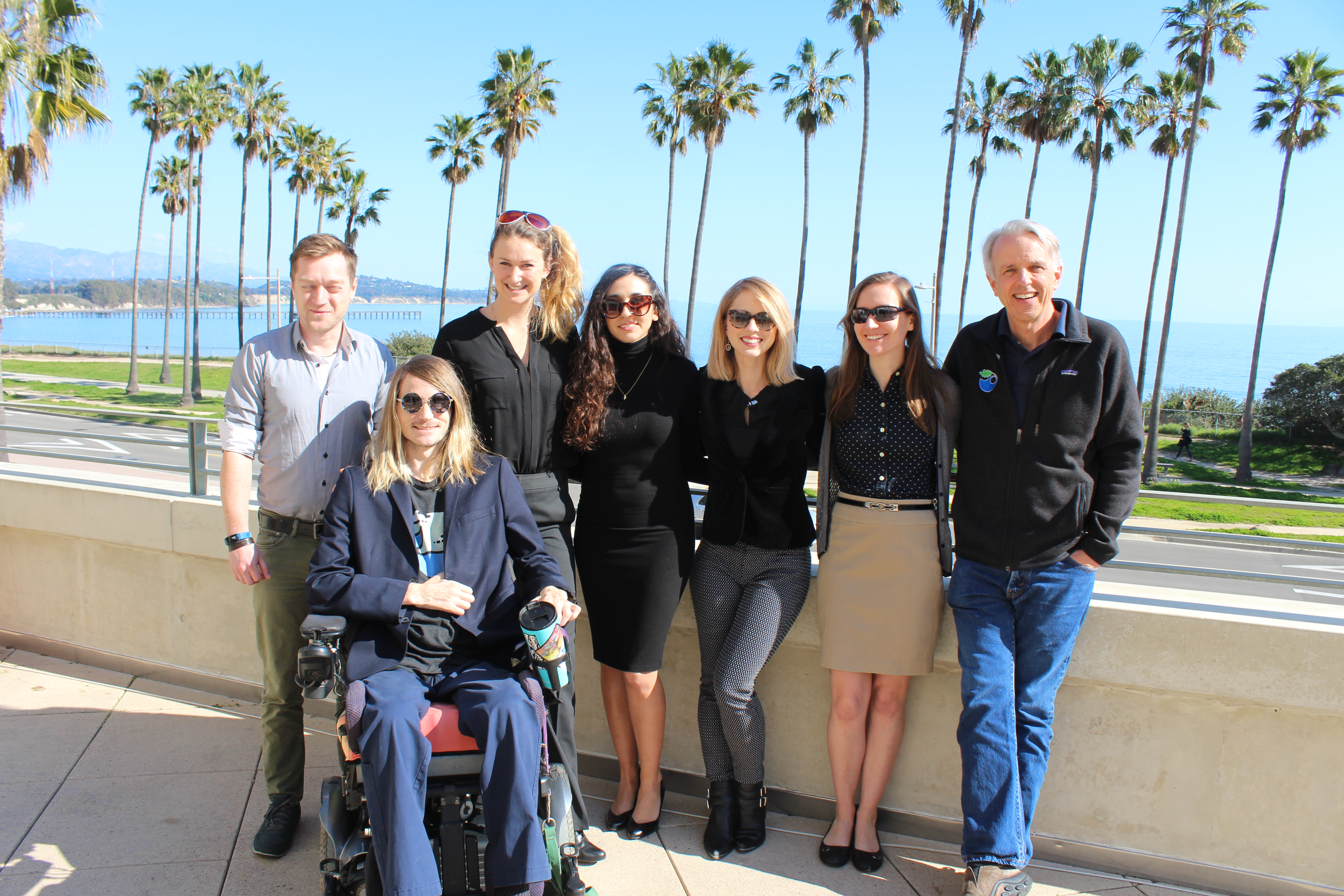 A student group poses with faculty and PhD advisors with an ocean backdrop