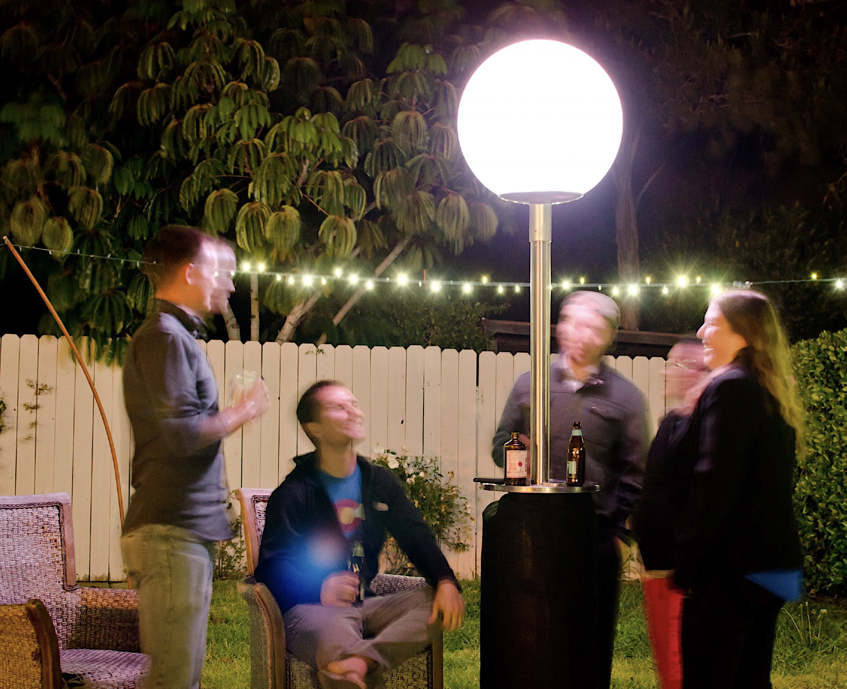 Four people sitting outdoors at night around a bright lamp