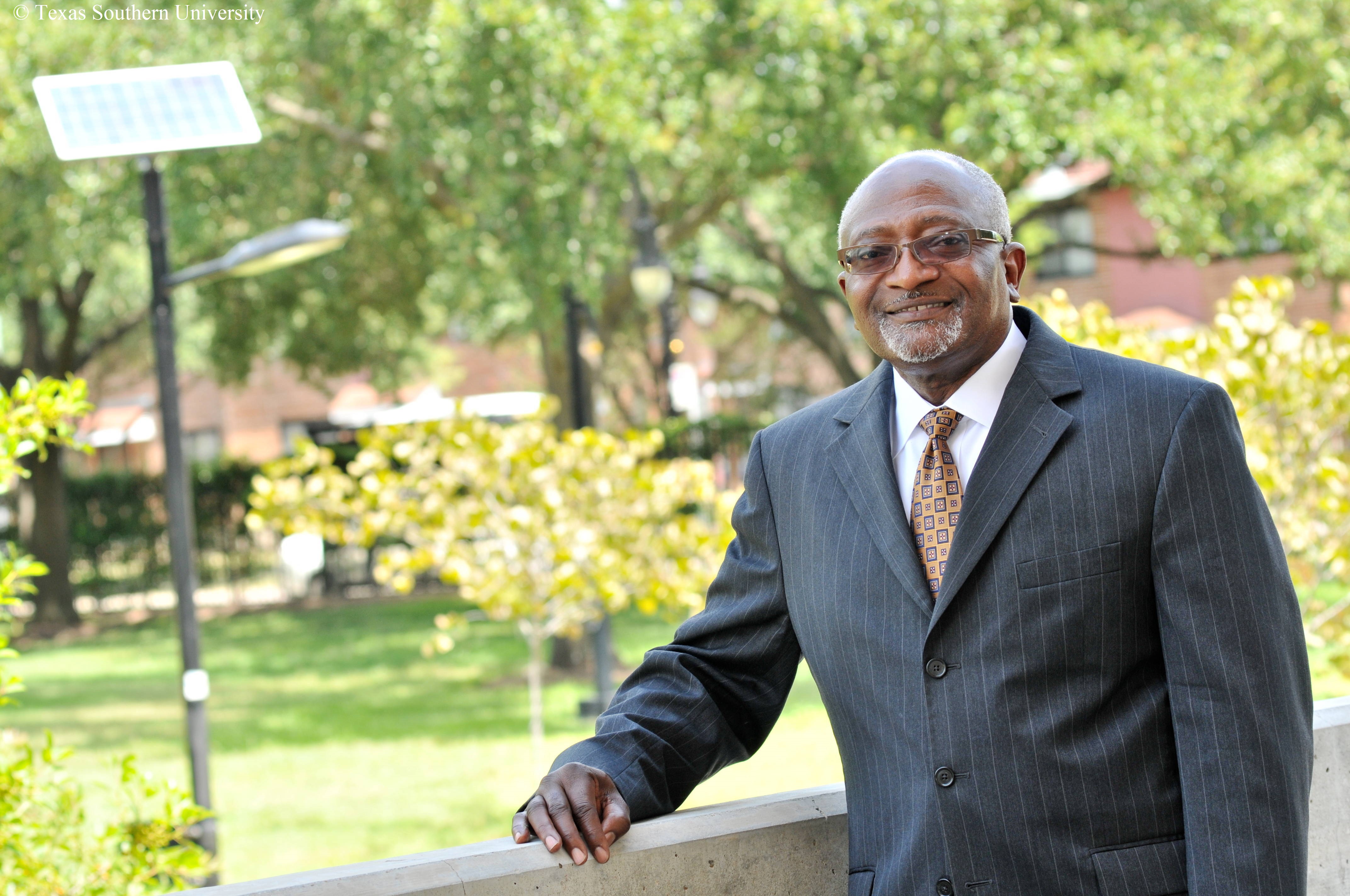 Robert Bullard stands with his hand on a railing in front of greenery