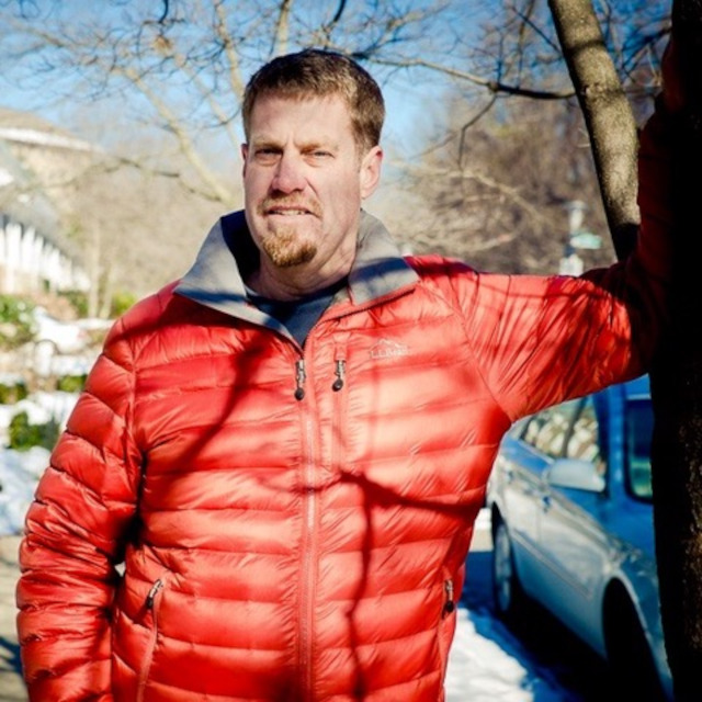 Morgan Grove wears an orange coat and stands next to a bare tree