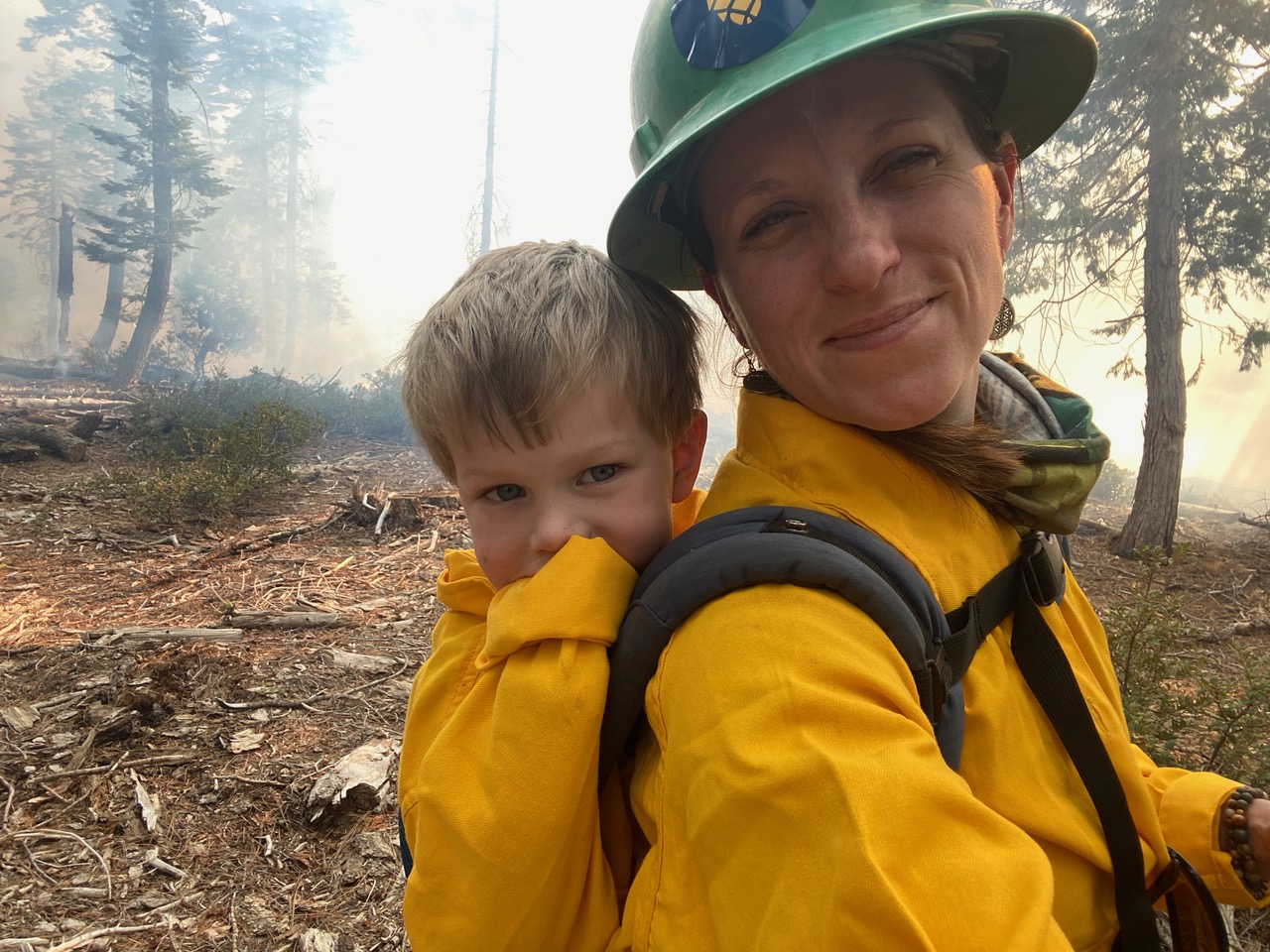 Sarah Bisbang stands with a child on her back in a forest