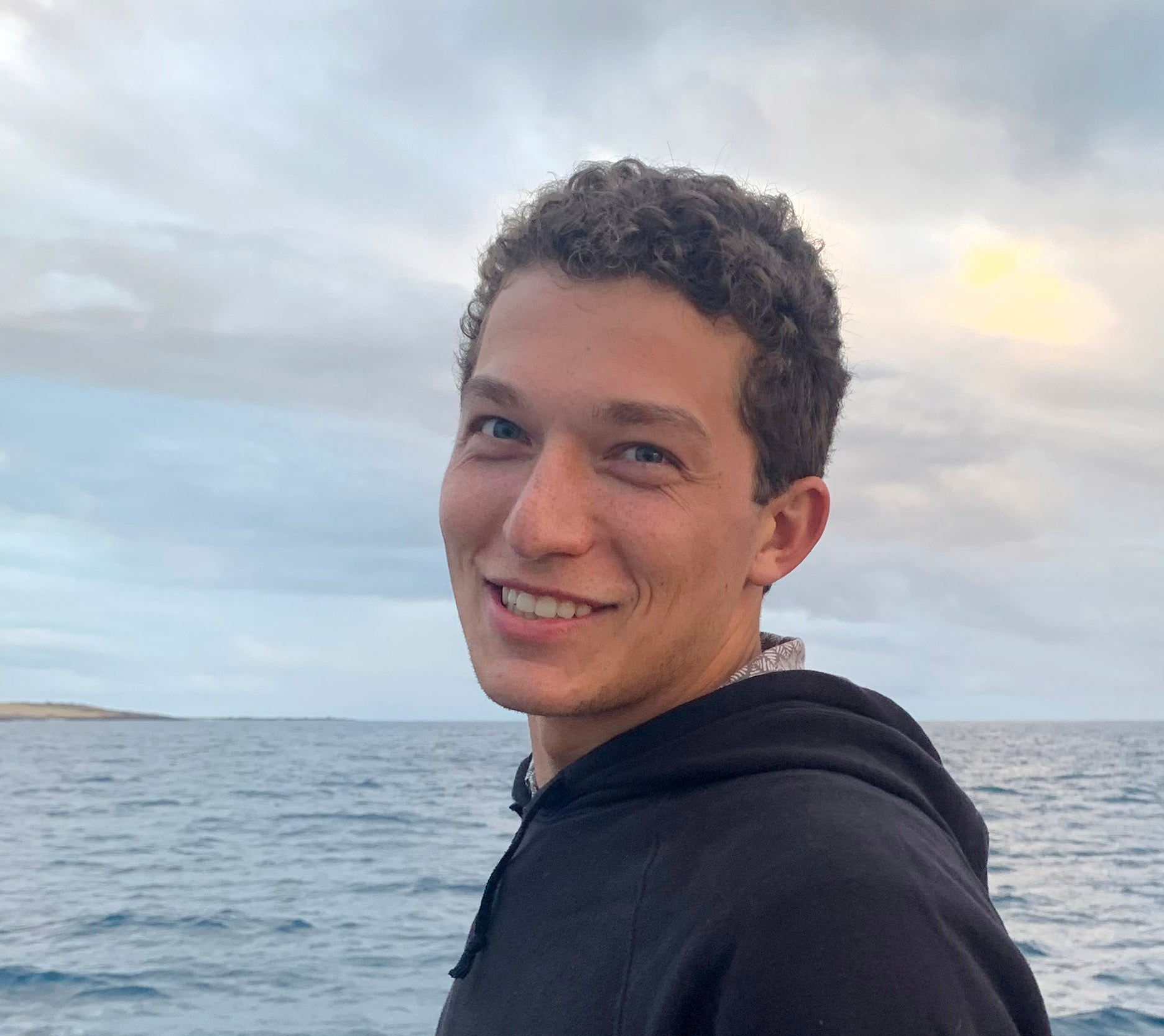 Person standing on boat with ocean in background, smiling
