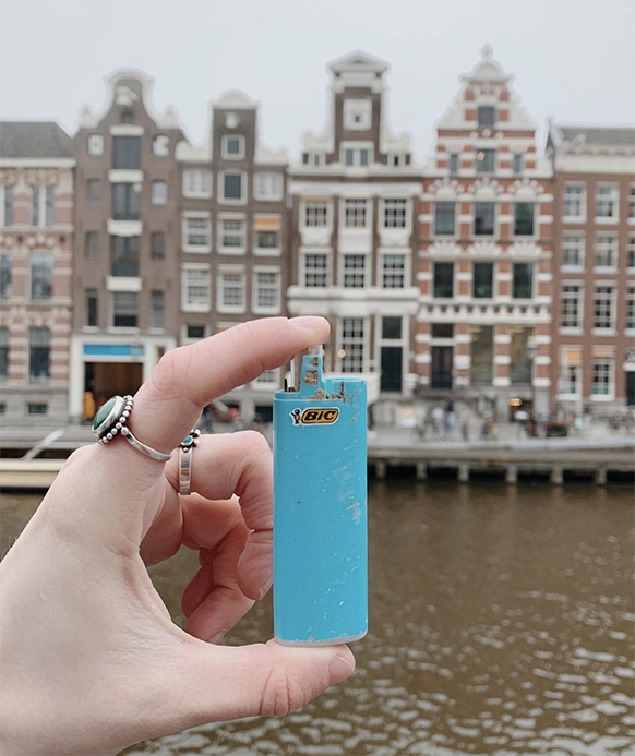 Hand holding up an old plastic lighter case with Amsterdam buildings in background