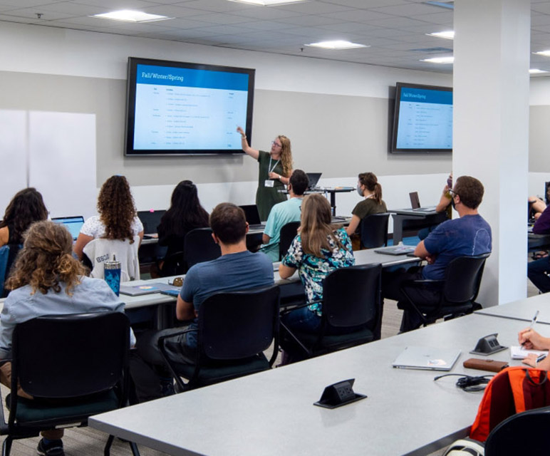 Room of students at desks watching an instructor at head of room