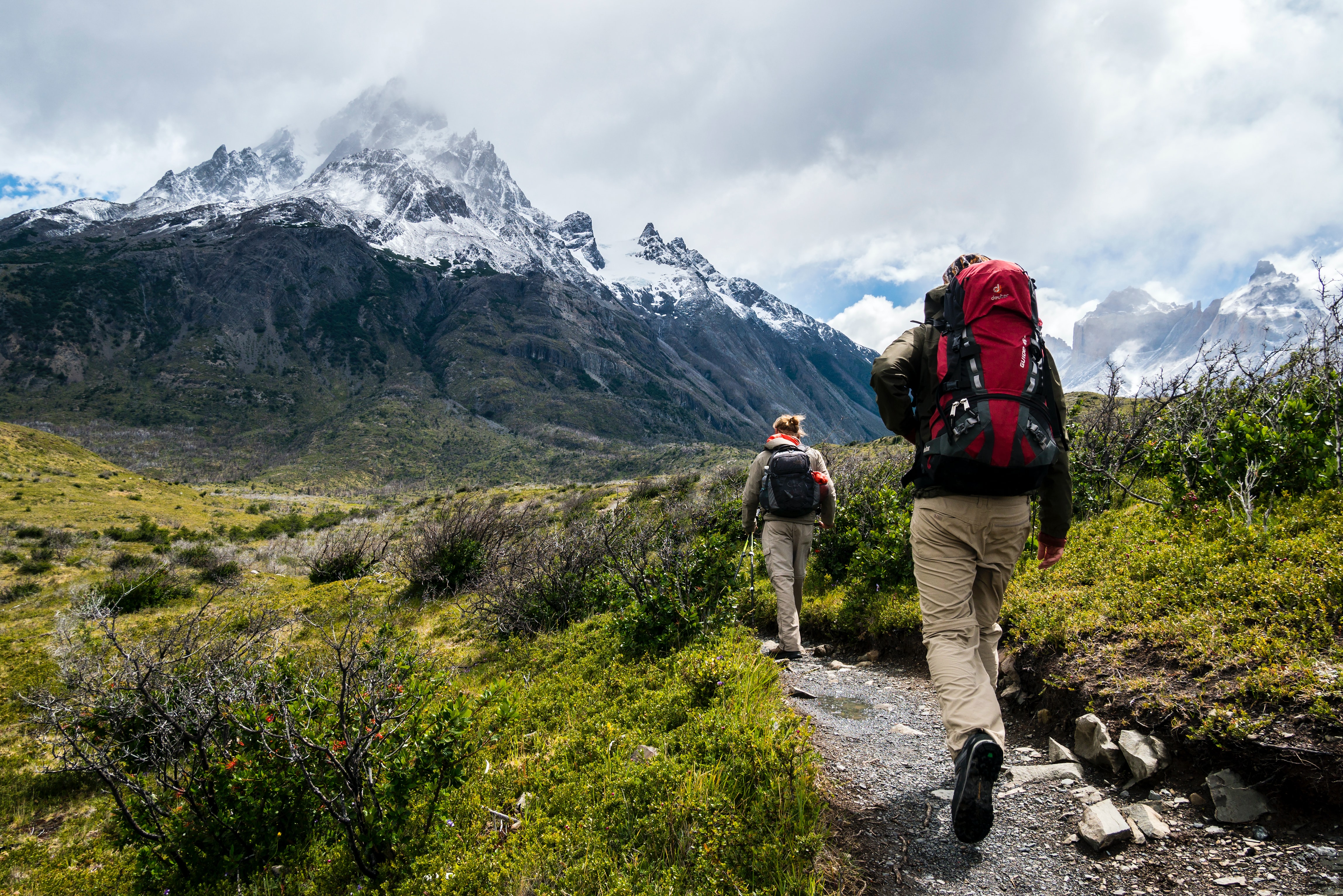 Woman and man hiking through valley, with snowcapped mountains.