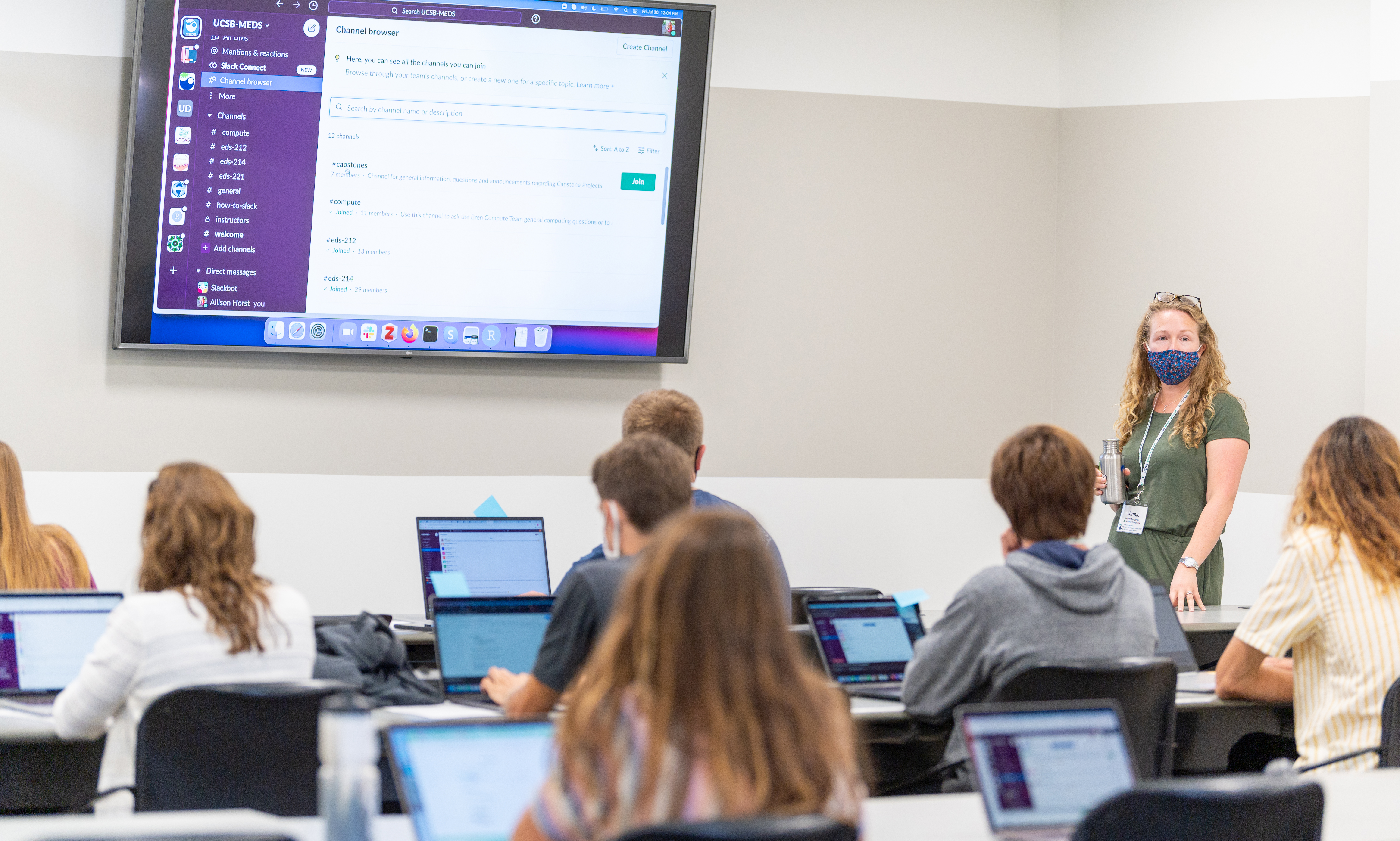 Woman stands in front of large monitor in classroom of students