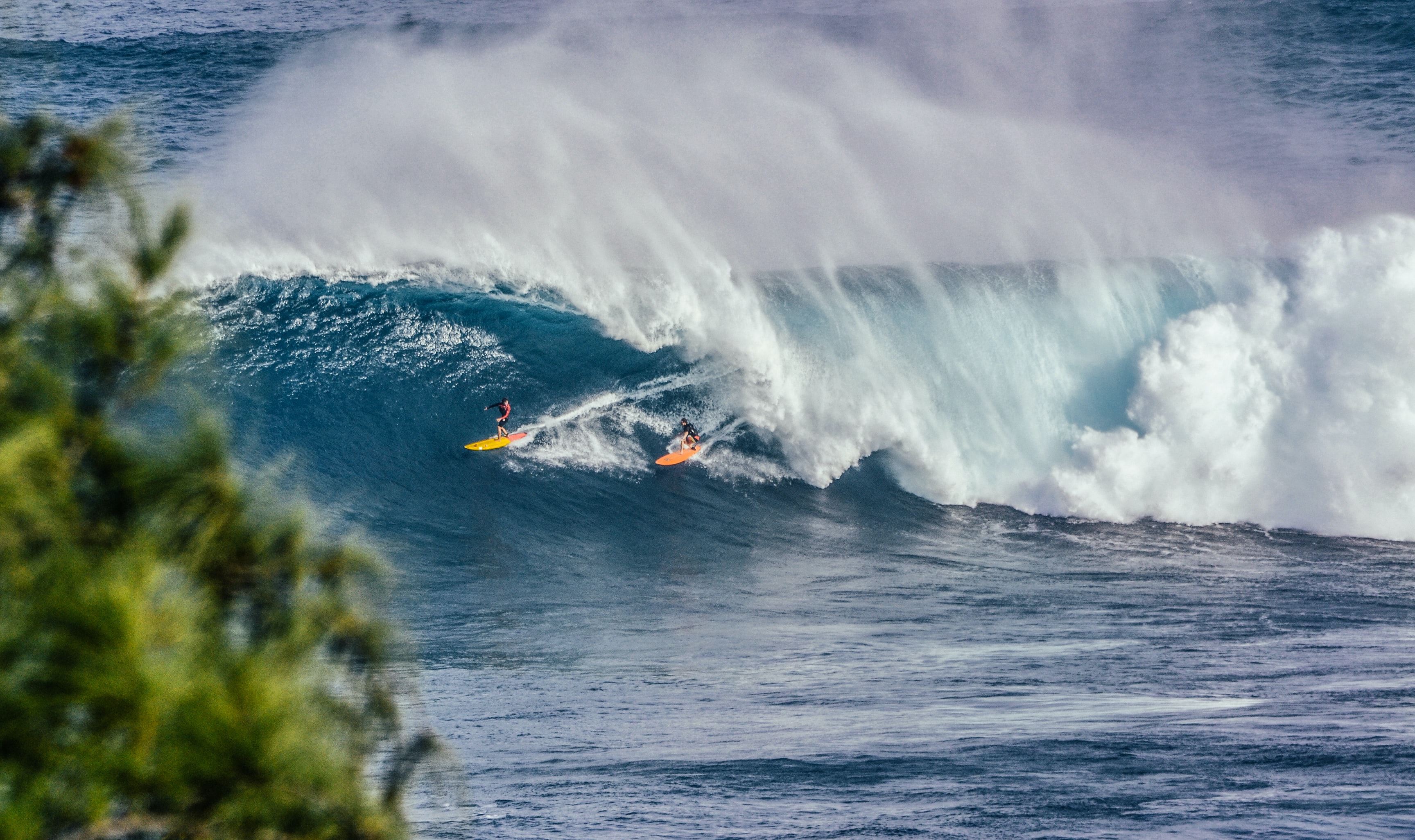 waves crashing on the coastline with two surfers on the wave.