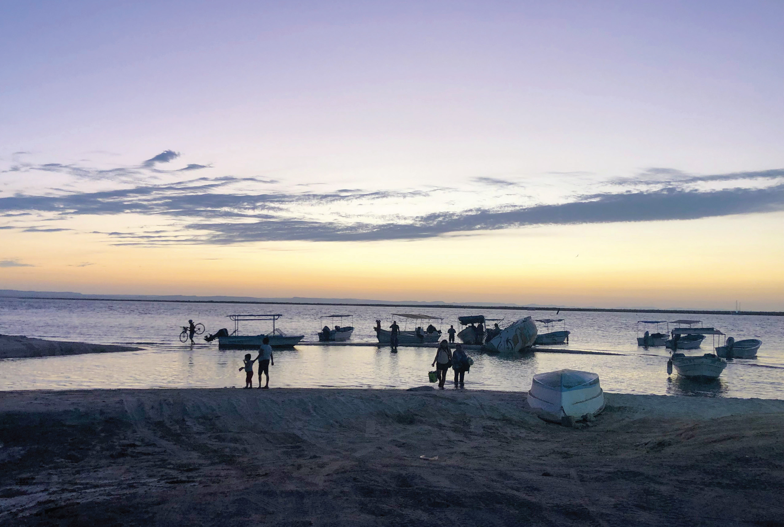 Twilight at a beach with boats close to shore and people silhouettes