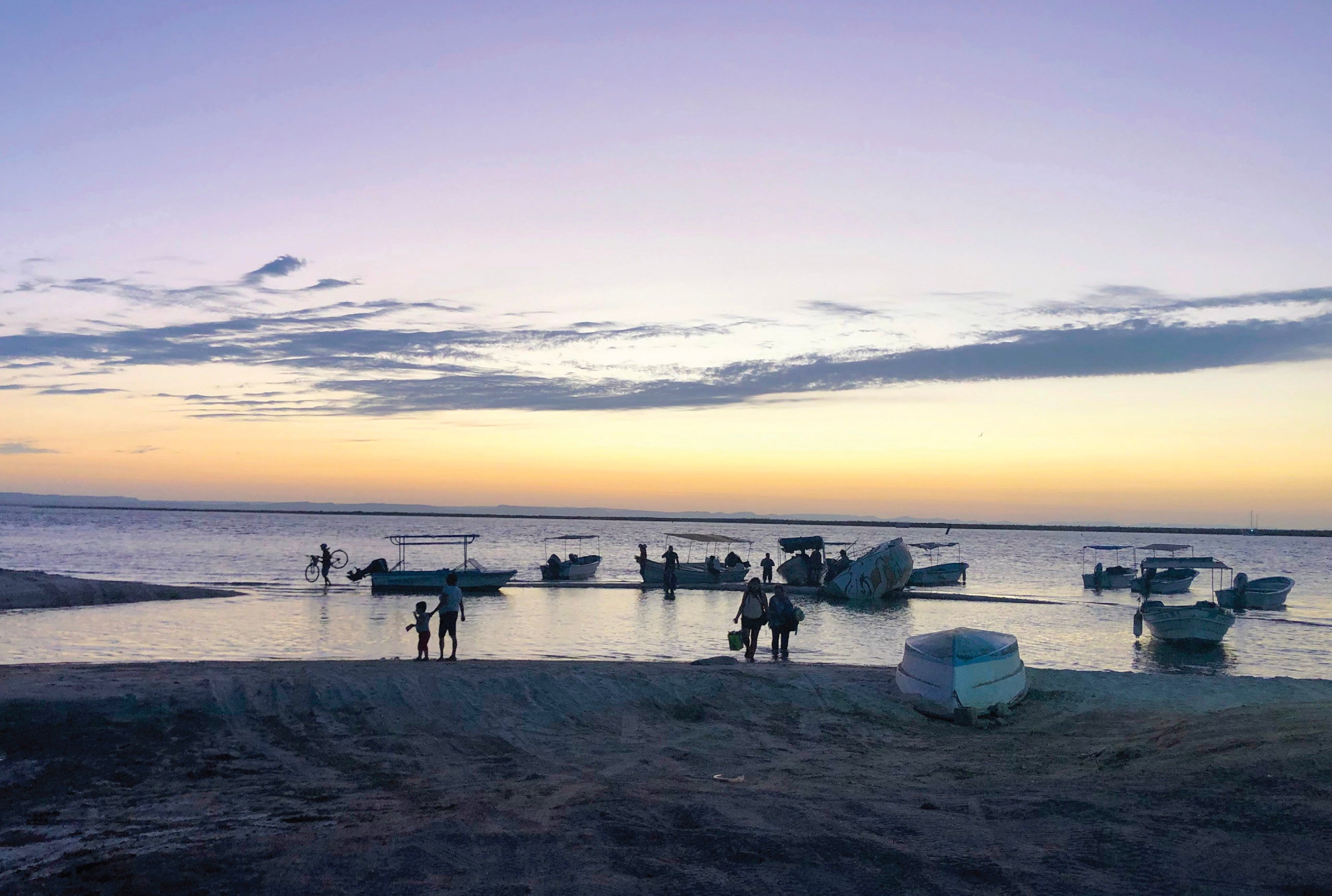 Twilight at a beach with boats close to shore and people silhouettes