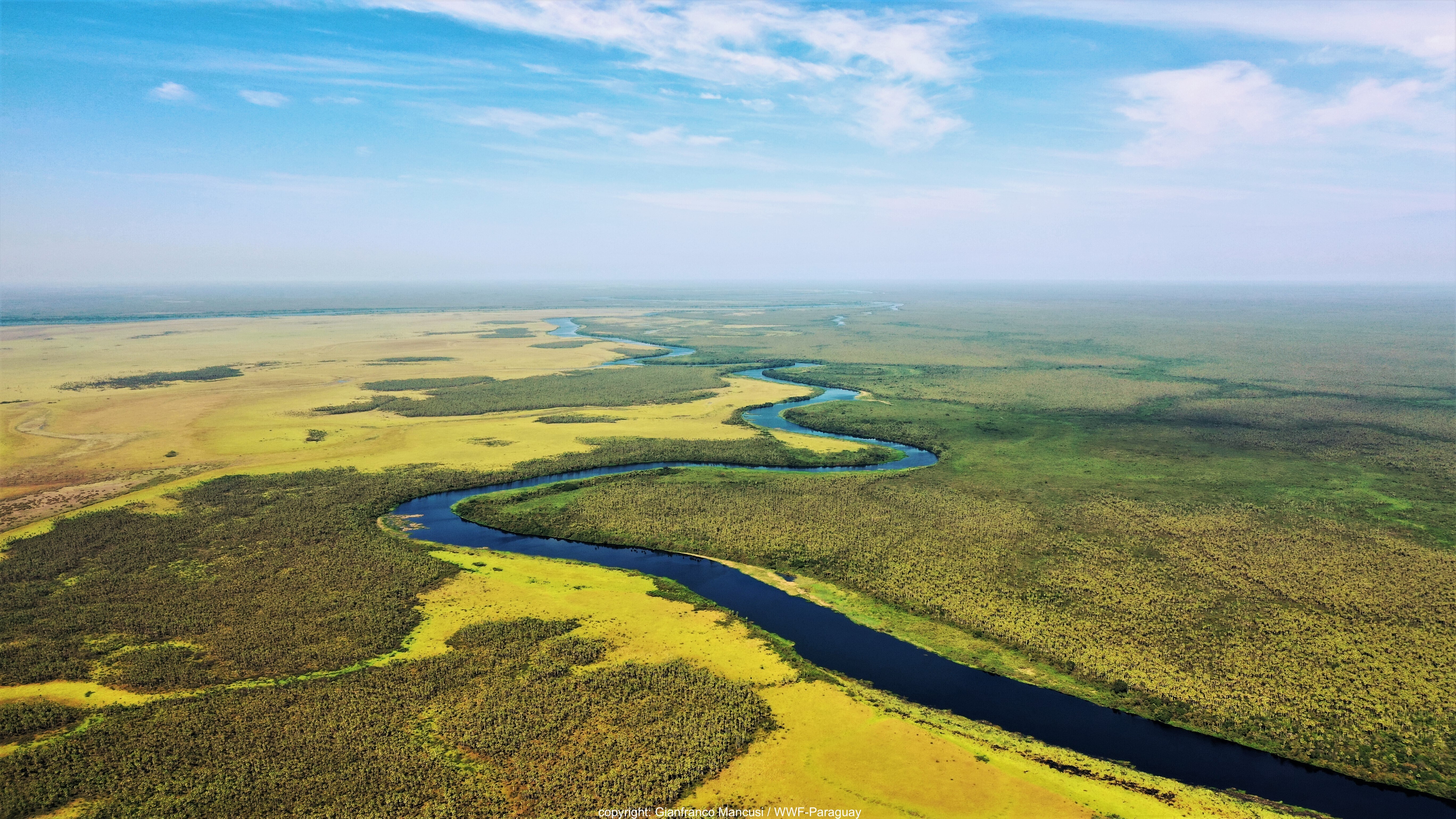 River running through a vast lush landscape, clouds in a blue sky 