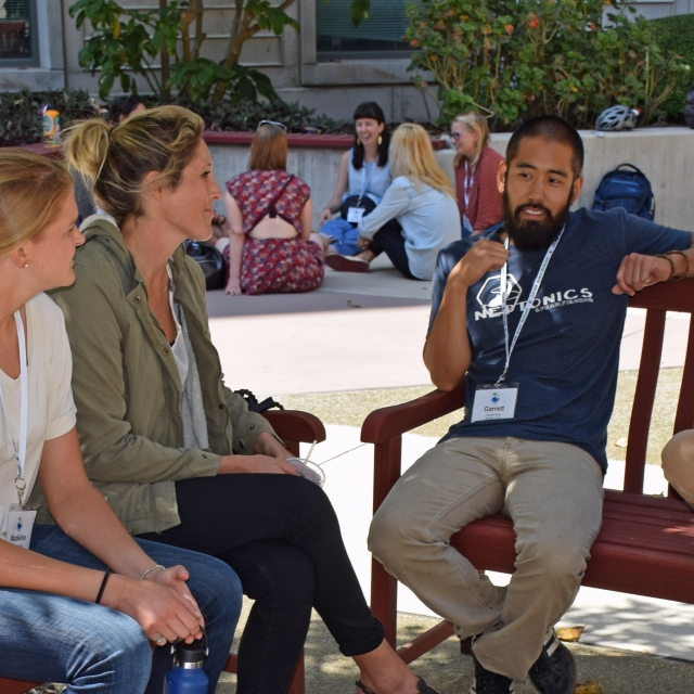 Five students having discussion on benches in sunny courtyard