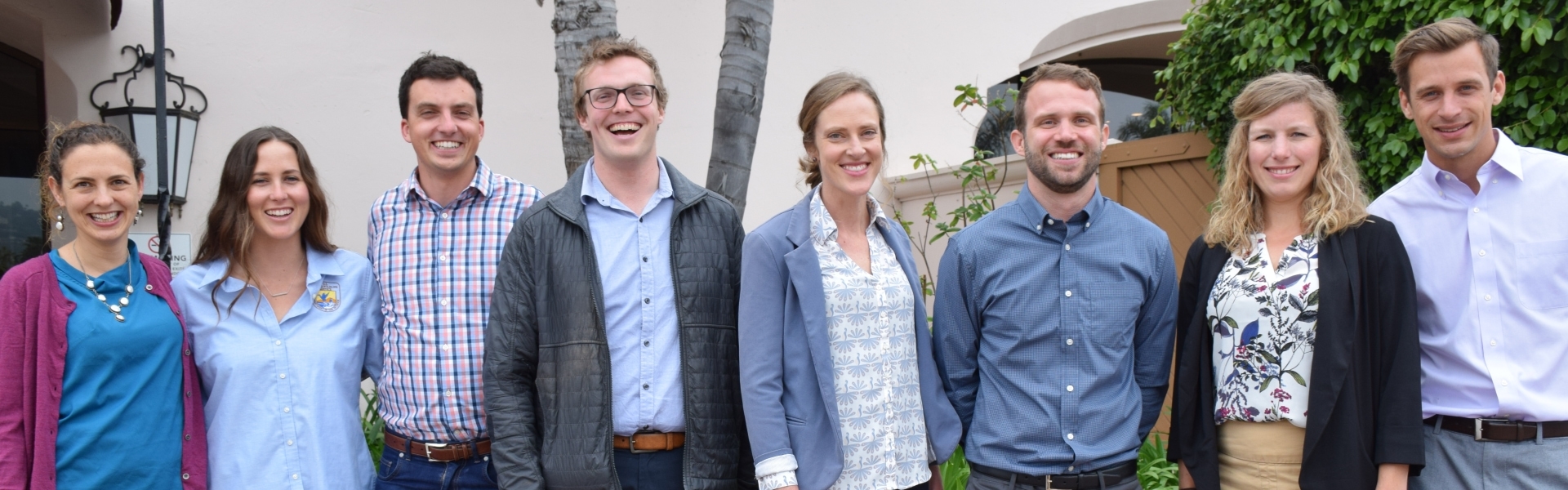 Group of eight people stand in row smiling