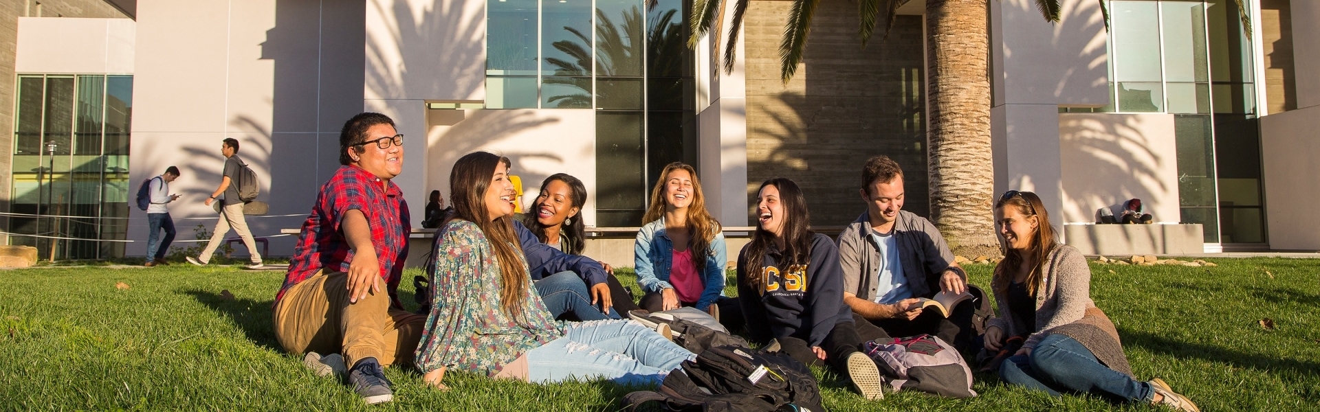 Seven students sitting in grass laughing