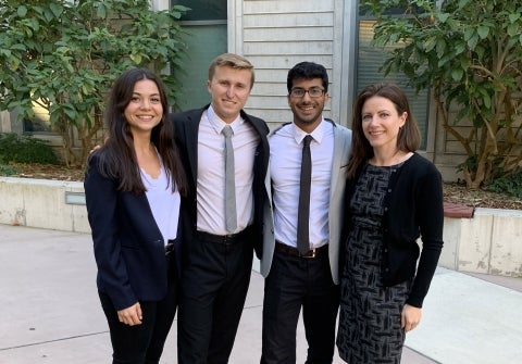Two women and two men in suits stand together in courtyard