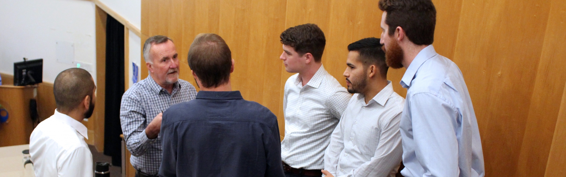 Five students stand while a professor talks to them