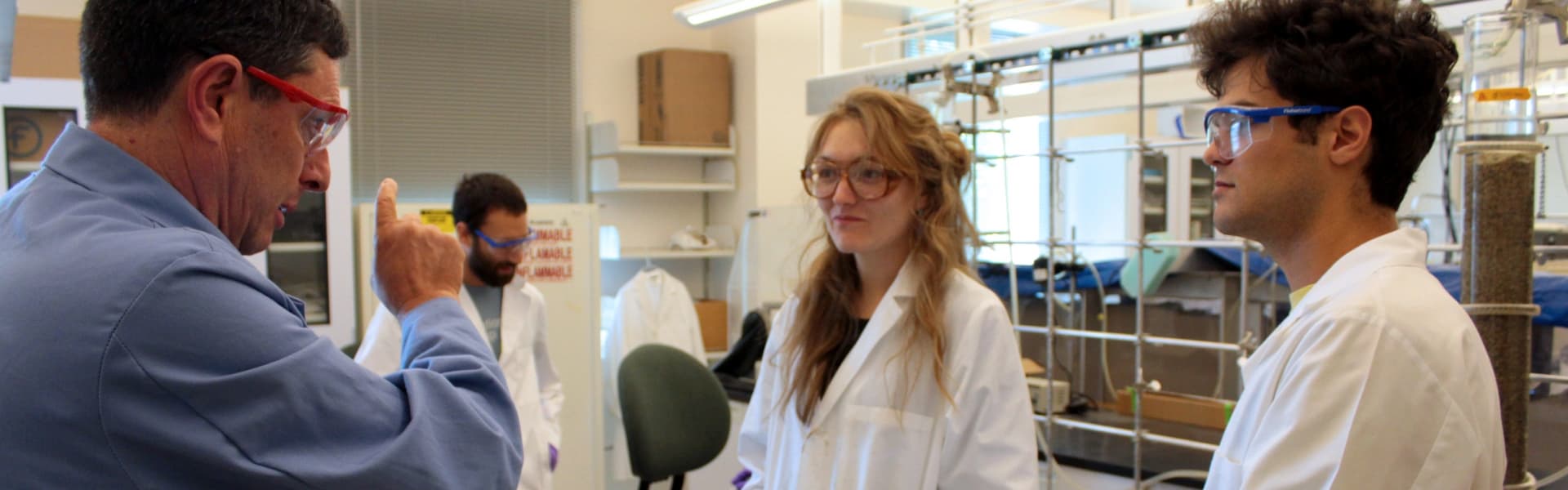 Professor instructs two researchers in lab coats in a laboratory