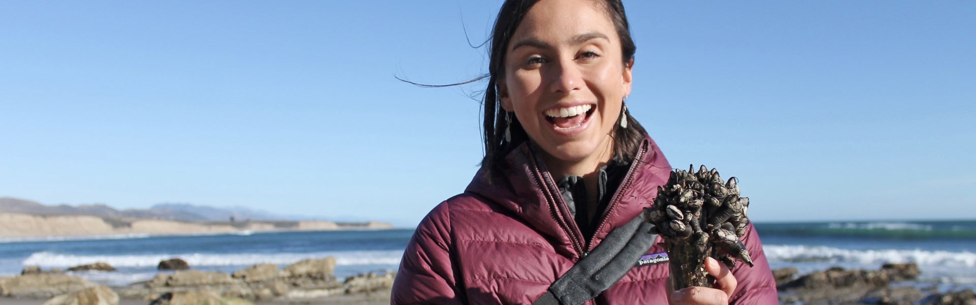 Woman holds up items found tidepooling on the beach