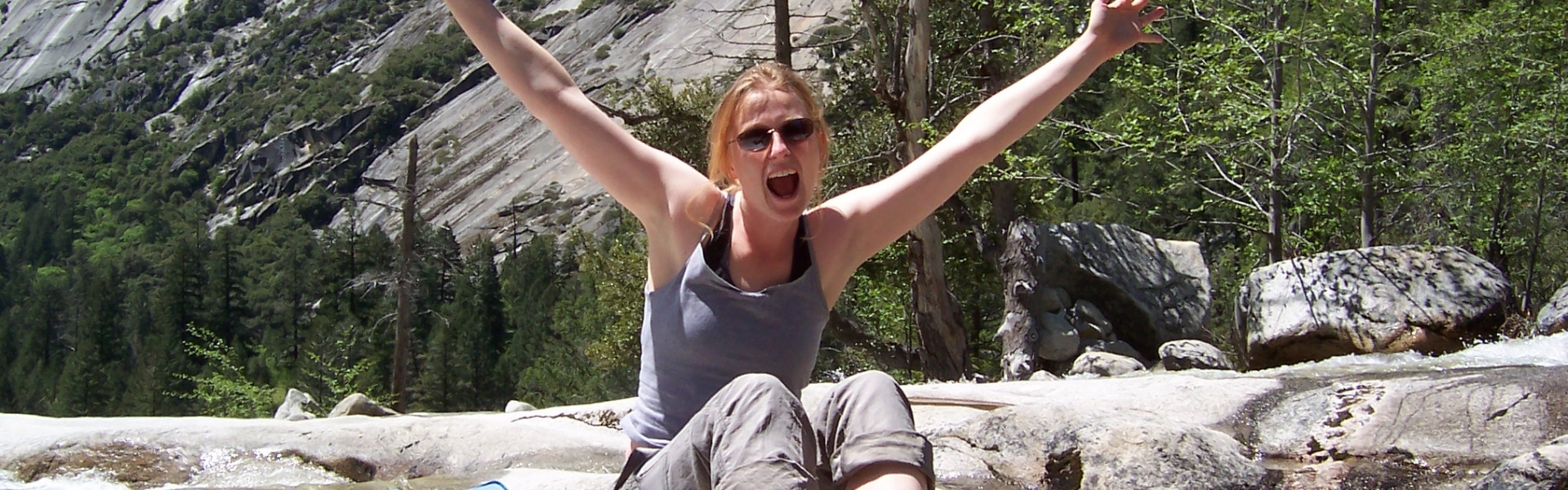 Woman sits on rock by river with happy expression