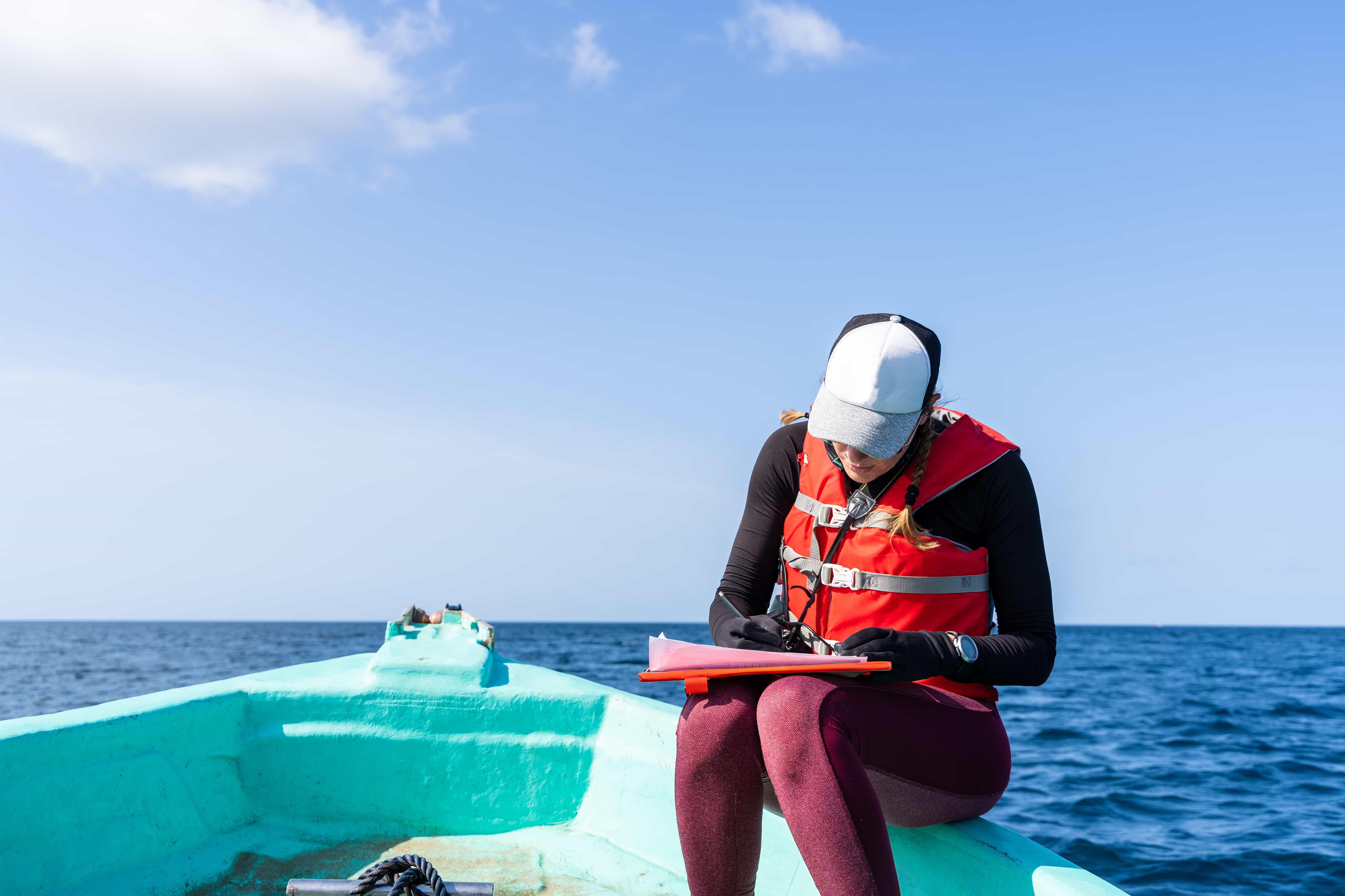 Marine biologist writing down data sitting on a boat