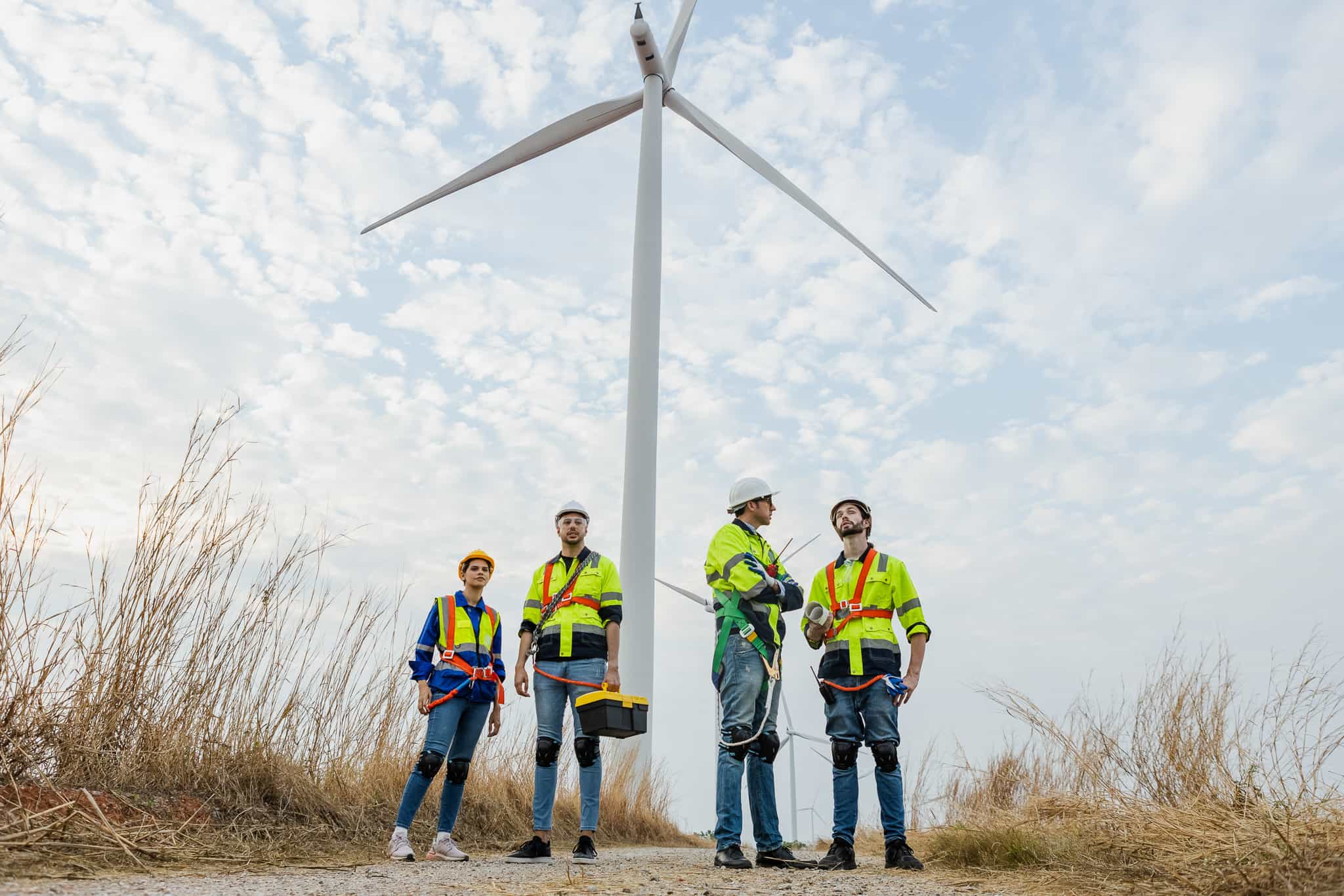 Teamwork engineer wearing safety uniform standing crossed arms at wind turbine