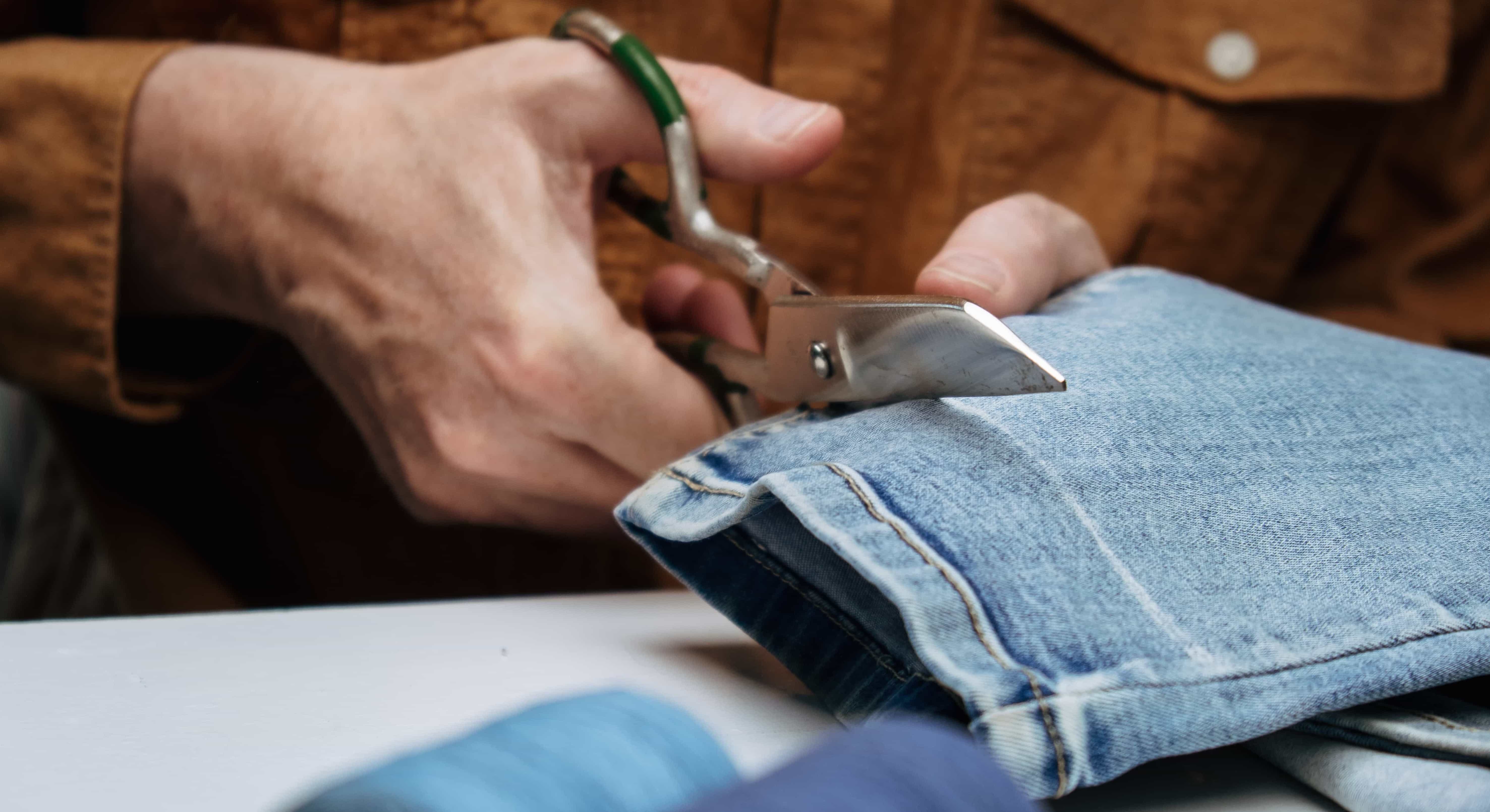 tailor in sewing studio works with jeans. cuts off the extra length of jeans with scissors. close-up