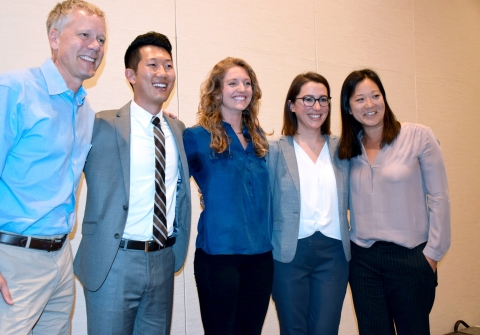 Five people link arms and smile on stage