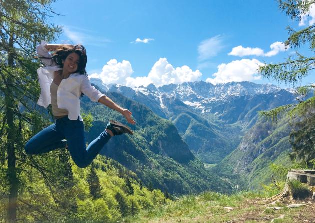 Woman jumping into air with forest mountain vista behind her