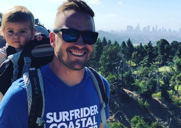 Hiking man with baby in backpack, city in distance