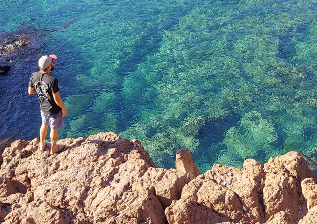 Man standing on rocks looking at clear ocean water