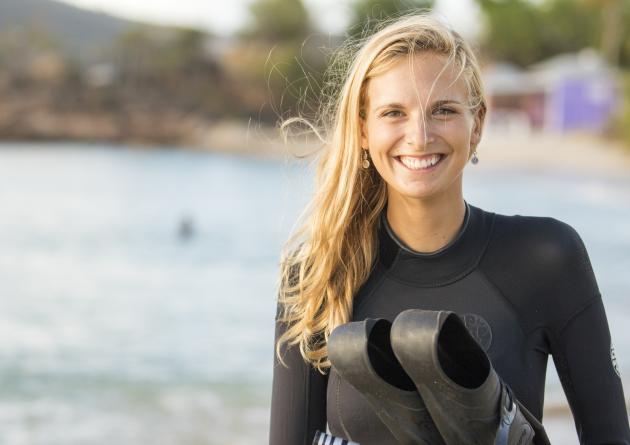 Molly Wilson stands on a beach holding swim fins