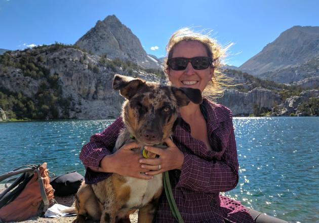 woman and dog sitting by a sparkling lake