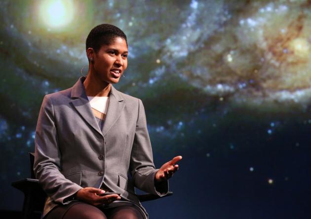 Woman giving talk on stage with space background