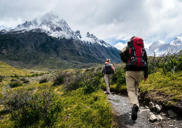 Woman and man hiking through valley, with snowcapped mountains.