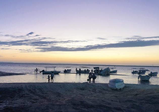 Twilight at a beach with boats close to shore and people silhouettes