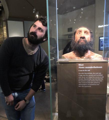 Man poses next to model of "neanderthal man" at museum