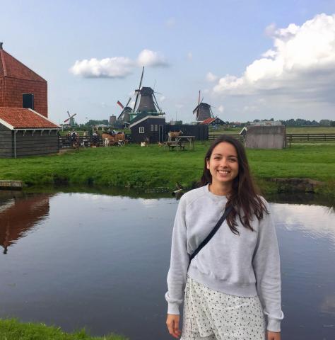 Woman stands in front of landscape with windmills and water