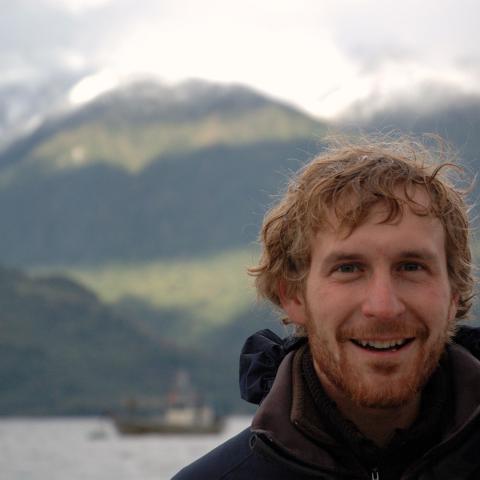 Man wearing warm jacket by lake with snowy hills in back