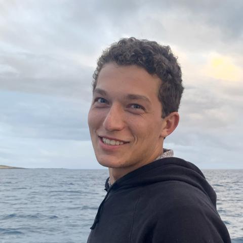 Person standing on boat with ocean in background, smiling