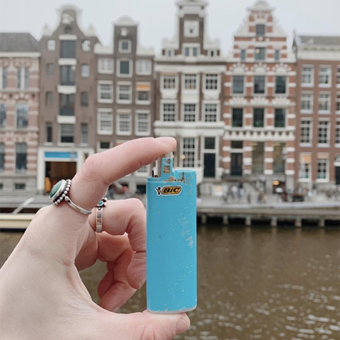 Hand holding up an old plastic lighter case with Amsterdam buildings in background