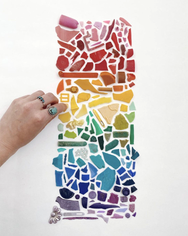 Hand placing plastic trash bits in a pattern forming a rainbow