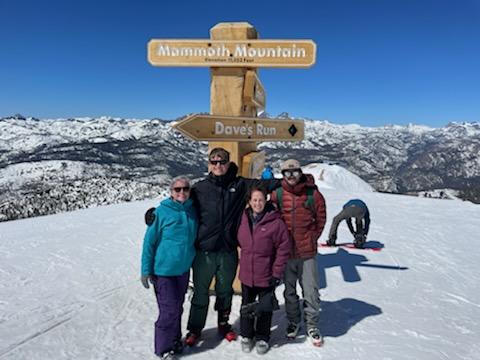 Four people on snowy mountain top pose in front of sign that reads Mammoth Mountain