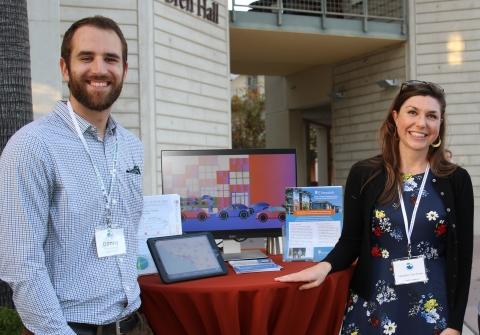 Two people stand by their media display at a tabling event