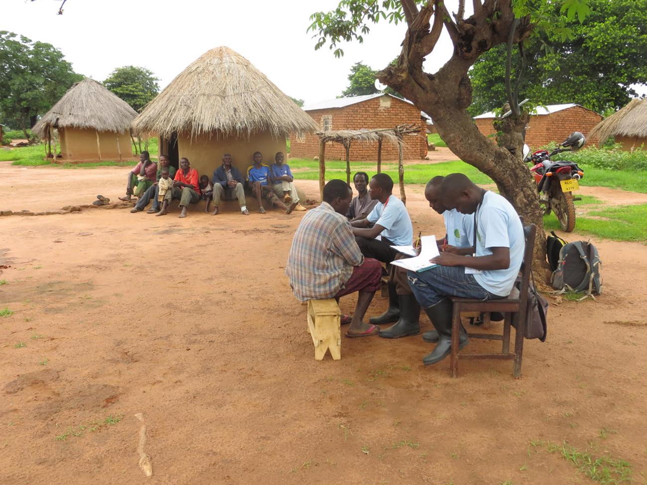 Group of Zambian farmers gathered on benches doing paperwork 